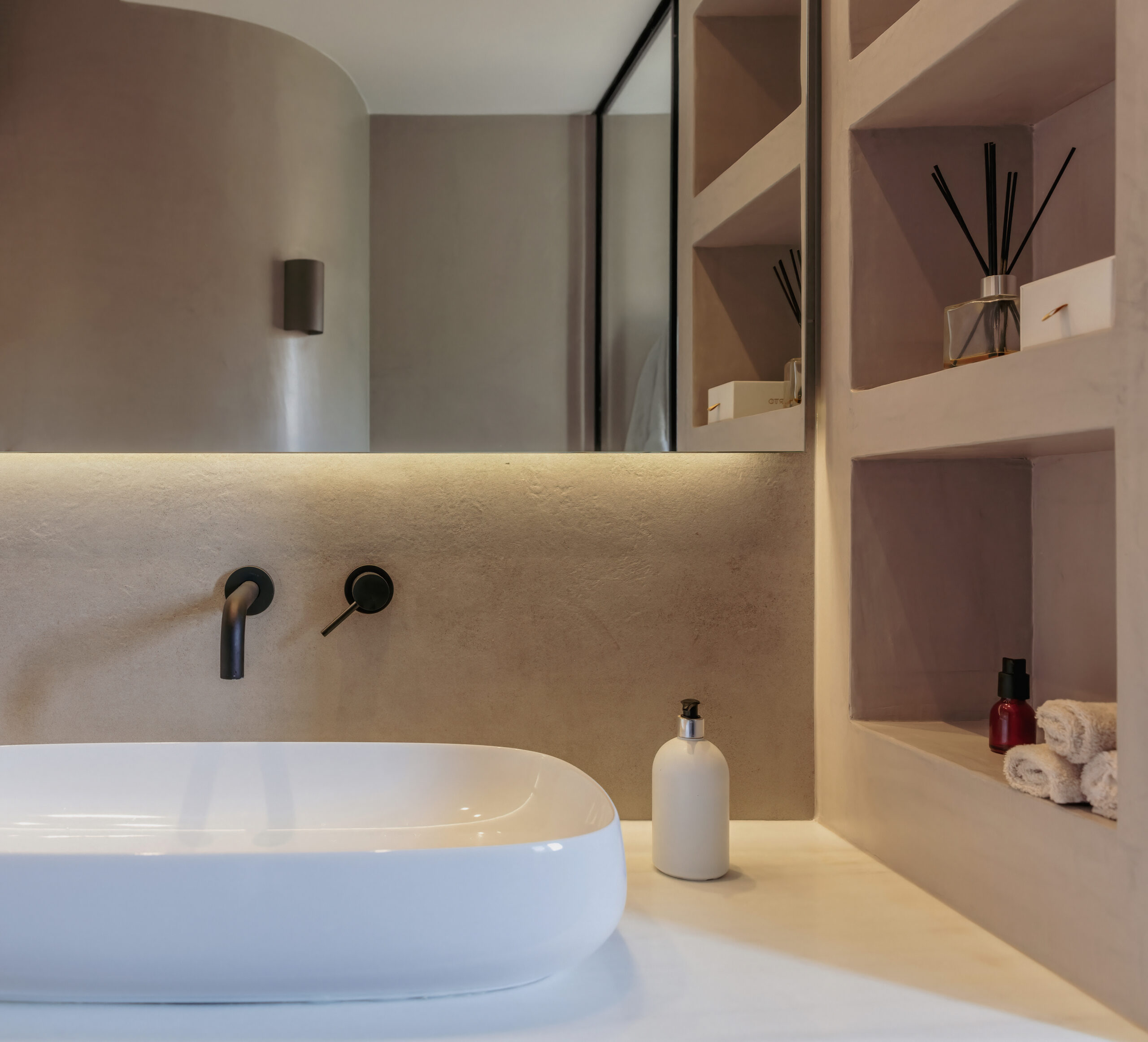 Bathroom vanity with a black wall-mounted faucet, curved plaster basin and a warm backlit niche