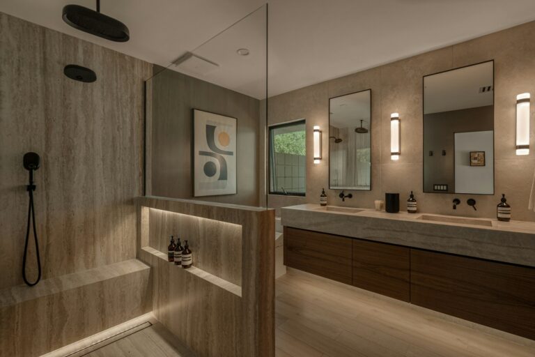 Travertine walk-in shower with a built-in bench, handheld shower and lit shelf beside a walnut vanity